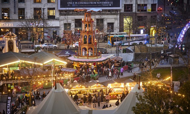 picture looking down on evening street scene with market stalls, lights twinkling a tall Christmas wooden windmill