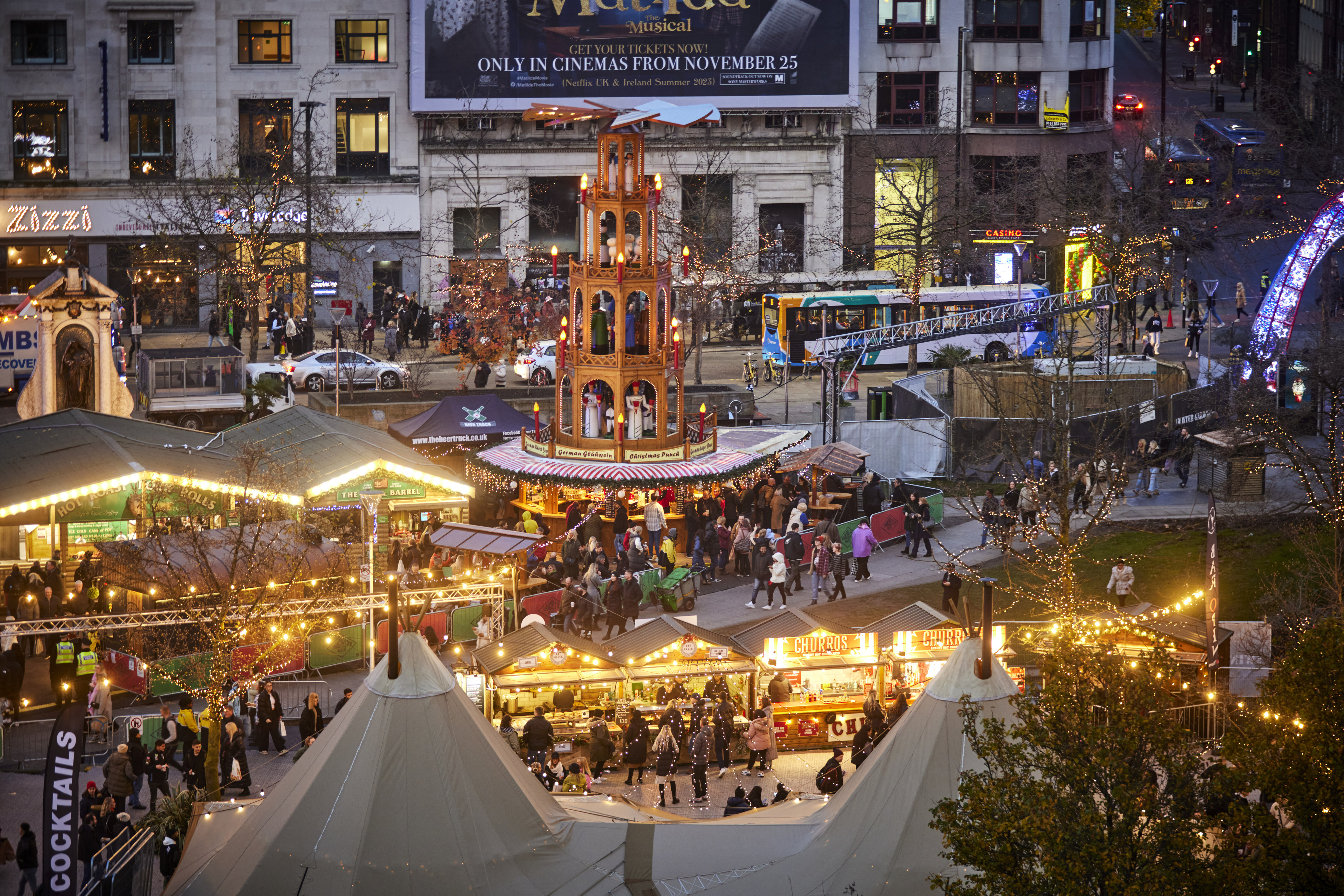 picture looking down on evening street scene with market stalls, lights twinkling a tall Christmas wooden windmill