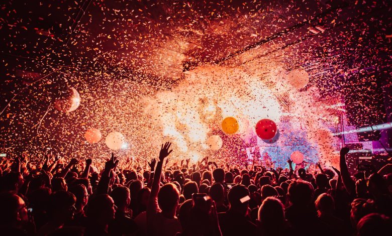 A crowd of people waving their arms in the air as they look towards a stage as balloons and confetti rain down.