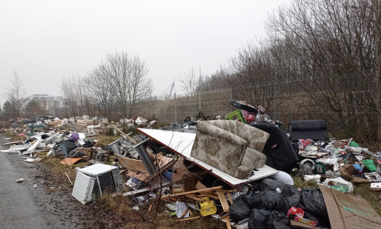 Image of a large pile of waste dumped by the side of the road. Items include a large sofa chair on top of other industrial waste.