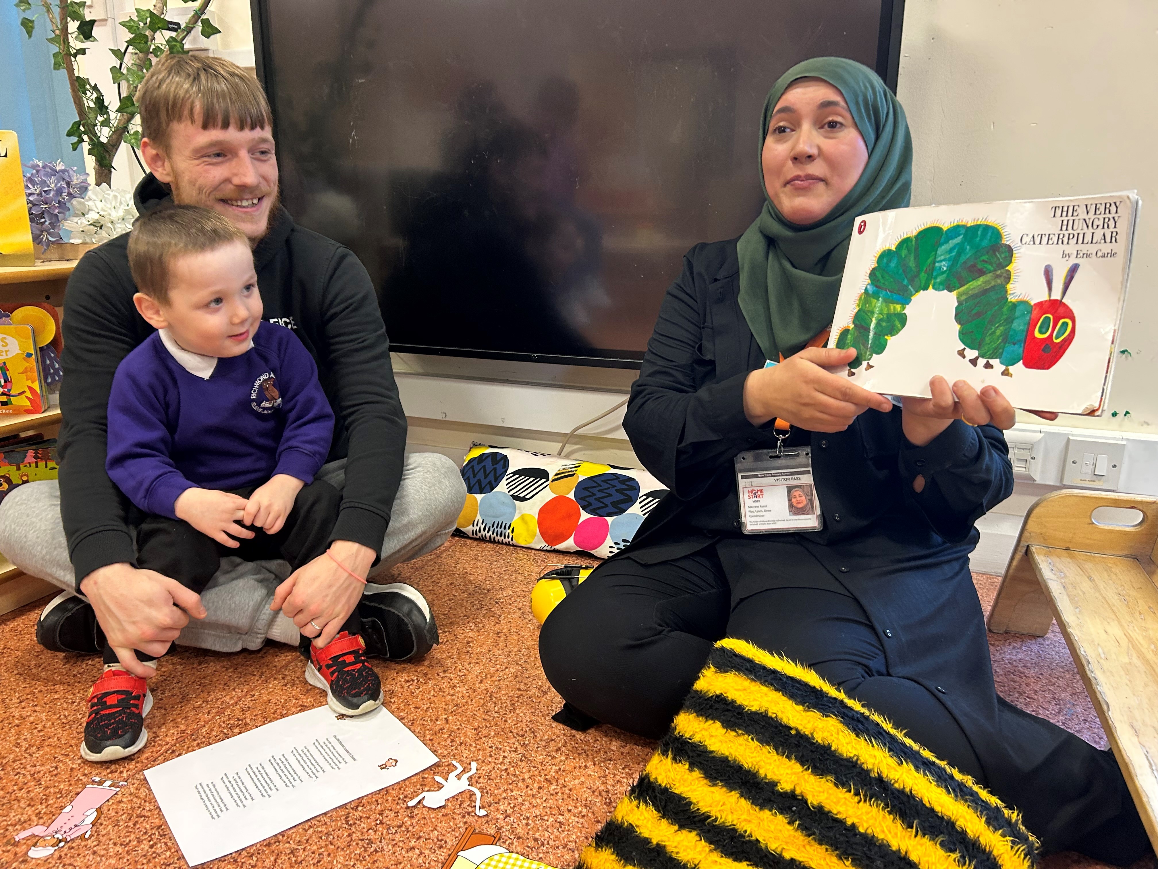 Joshua and his son smiling as they listen to a reading of the Hungry Caterpillar