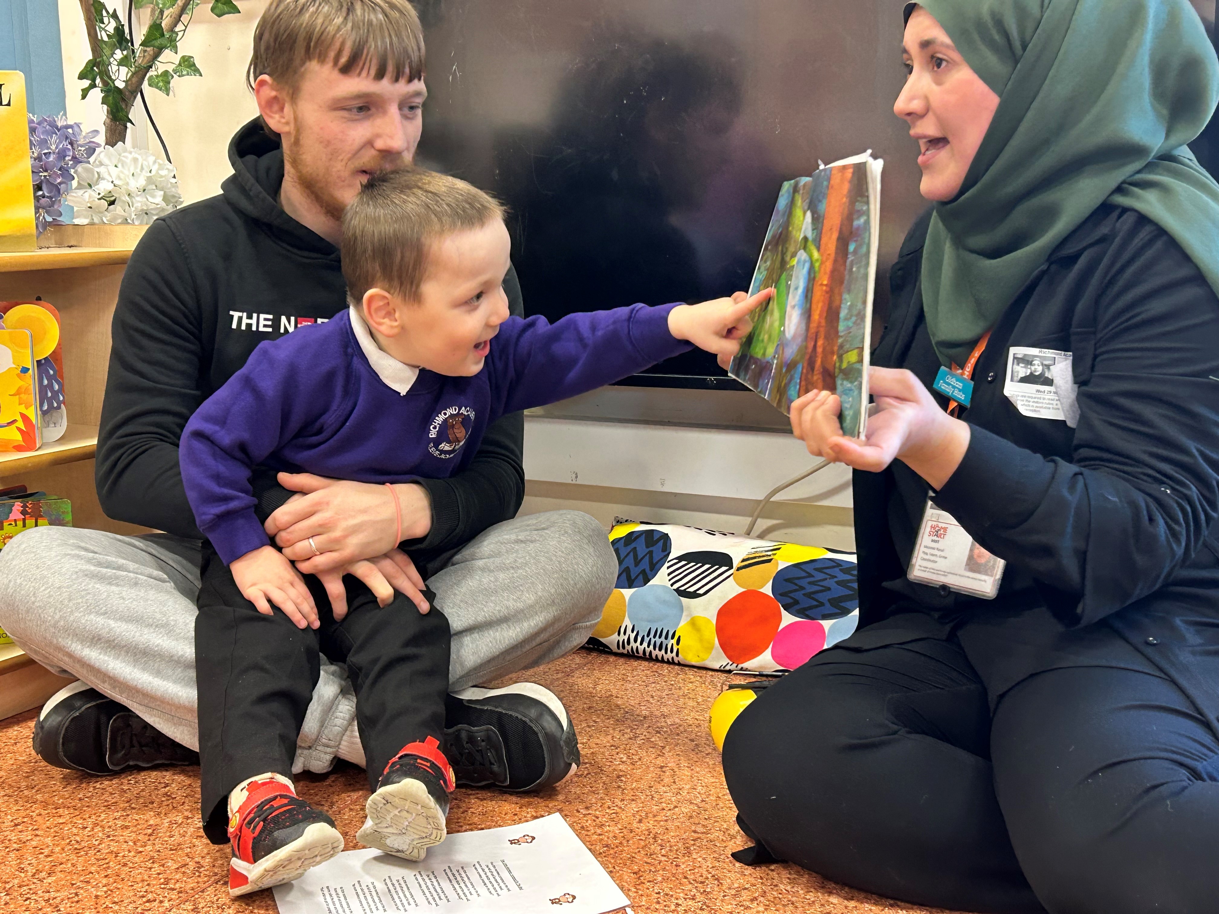 Joshua holding his son as he reads from a book