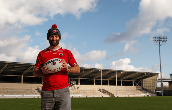 Salford City Mayor holding a rugby ball, stood on the pitch at the stadium