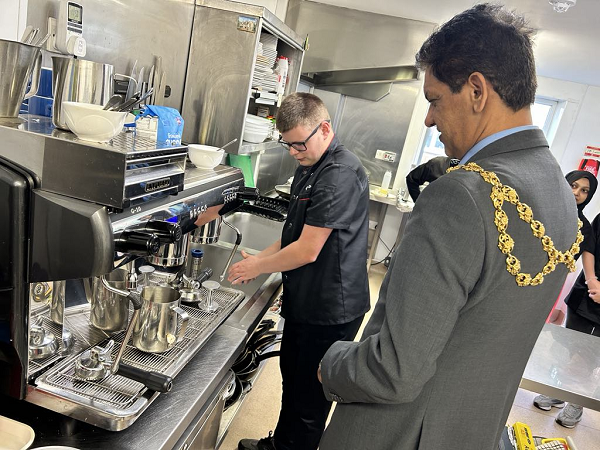 Volunteer Tyler showing Mayor of Oldham how to use barista machine.