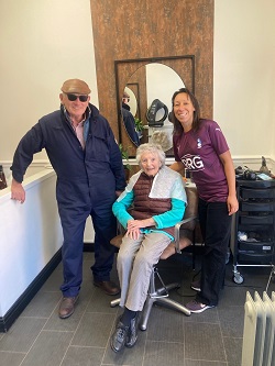 Mavis seated in a chair smiling with Frank Rothwell the owner of Oldham Athletic standing, also smiling, on her left