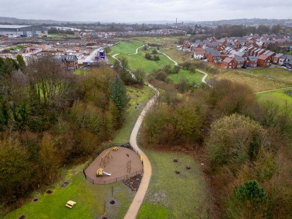 A drone shot of Broadway Green's park, with dozens of trees, a playground, a brook, and a pathway